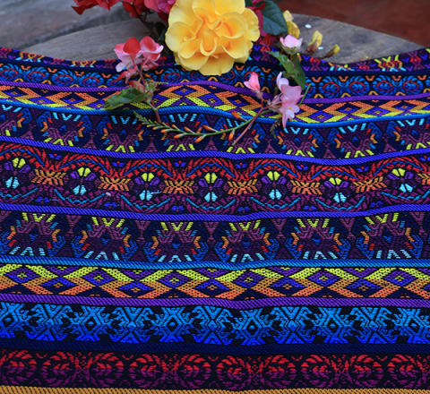 Güipil Kem Textiles, fondo: negro, con figuras en el centro de tonalidades rojo, corinto, anaranjado, amarillo, celeste y lila