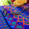 Güipil para niña, Kem Textiles, fondo: franjas azules, con figura geométrica en el centro de color magenta y anaranjado