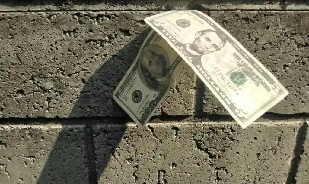 Dinero en billetes de diez y cinco dólares estadounidenses sobre suelo de ladrillo. – SoyMigrante.com REVISTA