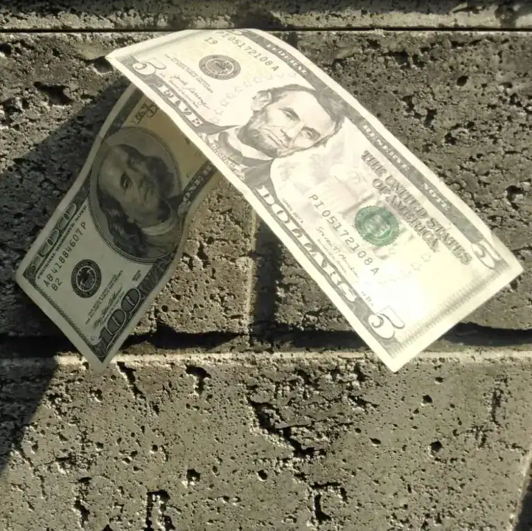 Dinero en billetes de diez y cinco dólares estadounidenses sobre suelo de ladrillo. – SoyMigrante.com REVISTA