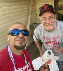 Manos con audífonos y gafas de sol en evento de migrantes en exteriores, sonriendo y mostrando actitud positiva. – SoyMigrante.com REVISTA