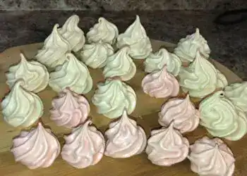 Bizcochos decorativos de merengue en colores blanco y rosado, ideales para repostería y pastelería creativa, presentados en una bandeja de madera, estilo artesanal y casero. – SoyMigrante.com REVISTA