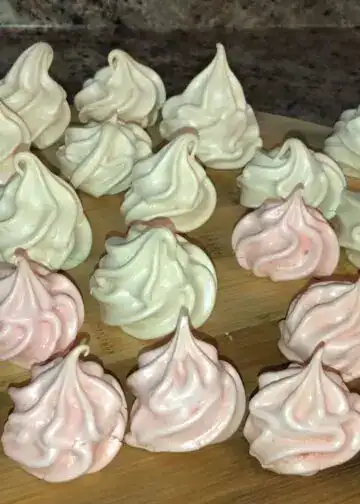 Bizcochos decorativos de merengue en colores blanco y rosado, ideales para repostería y pastelería creativa, presentados en una bandeja de madera, estilo artesanal y casero. – SoyMigrante.com REVISTA