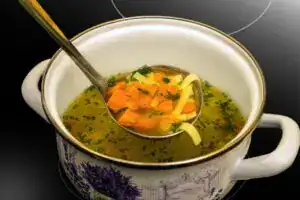 Receta chapina caldo de res al estilo guatemalteco. Caldo de verduras, sopa nutritiva y saludable con zanahorias, pasta y hierbas frescas en una taza artesanal. – SoyMigrante.com REVISTA