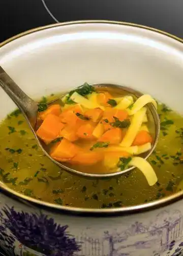 Receta chapina caldo de res al estilo guatemalteco. Caldo de verduras, sopa nutritiva y saludable con zanahorias, pasta y hierbas frescas en una taza artesanal. – SoyMigrante.com REVISTA