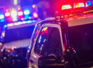 Accidente de tráfico con sirenas policiales en la noche en una ciudad. Vehículos de emergencia con luces azules y rojas activadas en una escena de accidente vial. – SoyMigrante.com REVISTA