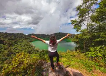 Espejo de agua en medio de la selva en un paisaje natural, mujer con los brazos abiertos disfrutando vista panorámica en un destino ecoturístico, turismo de naturaleza y aventuras en Latinoamérica.