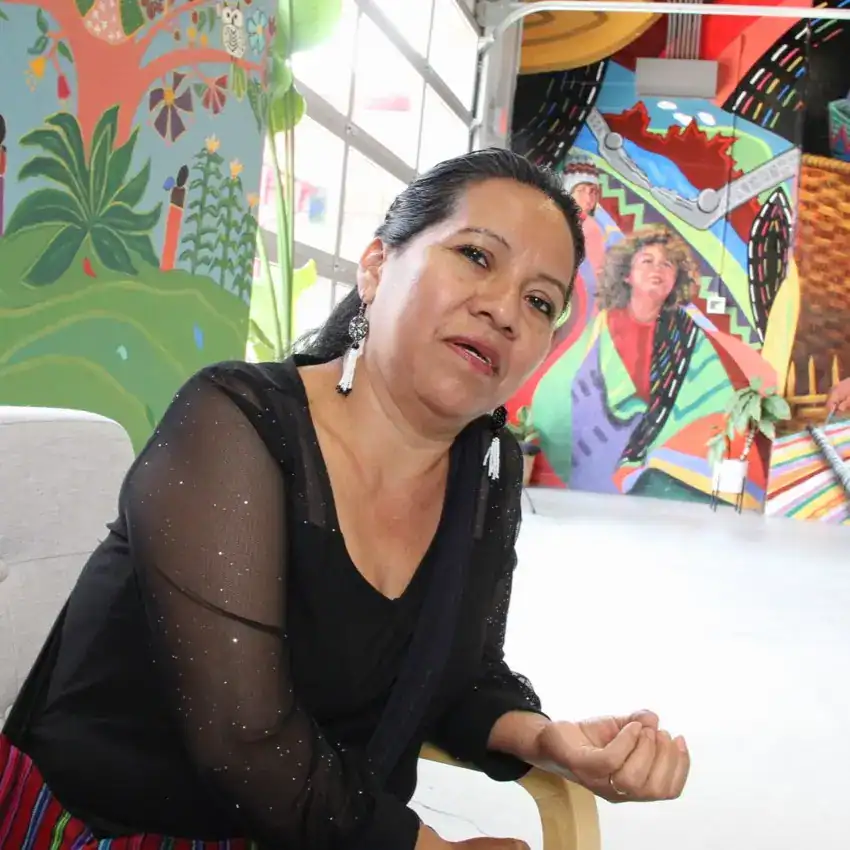 Retrato de mujer en evento cultural con murales coloridos en el fondo, promoviendo la diversidad y la creatividad en la comunidad migrante.