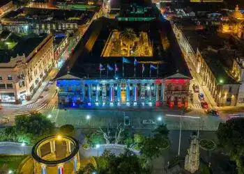 Majestuoso edificio histórico iluminado con luces de los colores de la bandera nacional en una ciudad animada por la noche, destacando la cultura y el patrimonio en el centro urbano.