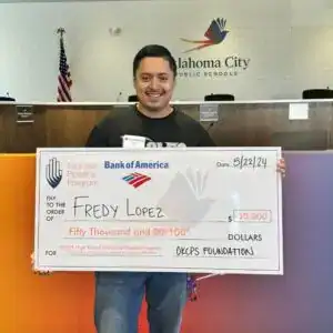 Premio de beca por ,000 a Fredy Lopez en la escuela OKCPS, evento destacado de solidaridad y apoyo a migrantes en Oklahoma City, con fondo de aula y logotipo de la ciudad. – SoyMigrante.com REVISTA