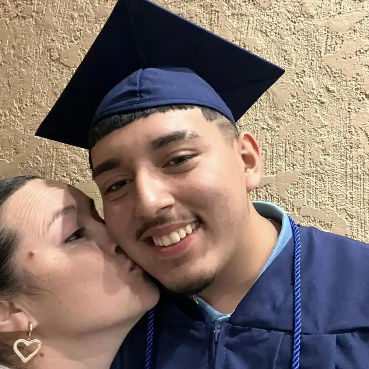 Graduación de migrantes, joven universitario con toga y birrete, celebración y orgullo académico, inclusión y éxito a través de la educación en la comunidad migrante.