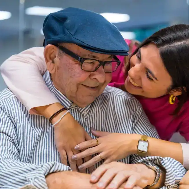 Adulto mayor y joven en un abrazo afectuoso en un ambiente de comunidad y apoyo para migrantes. – SoyMigrante.com REVISTA