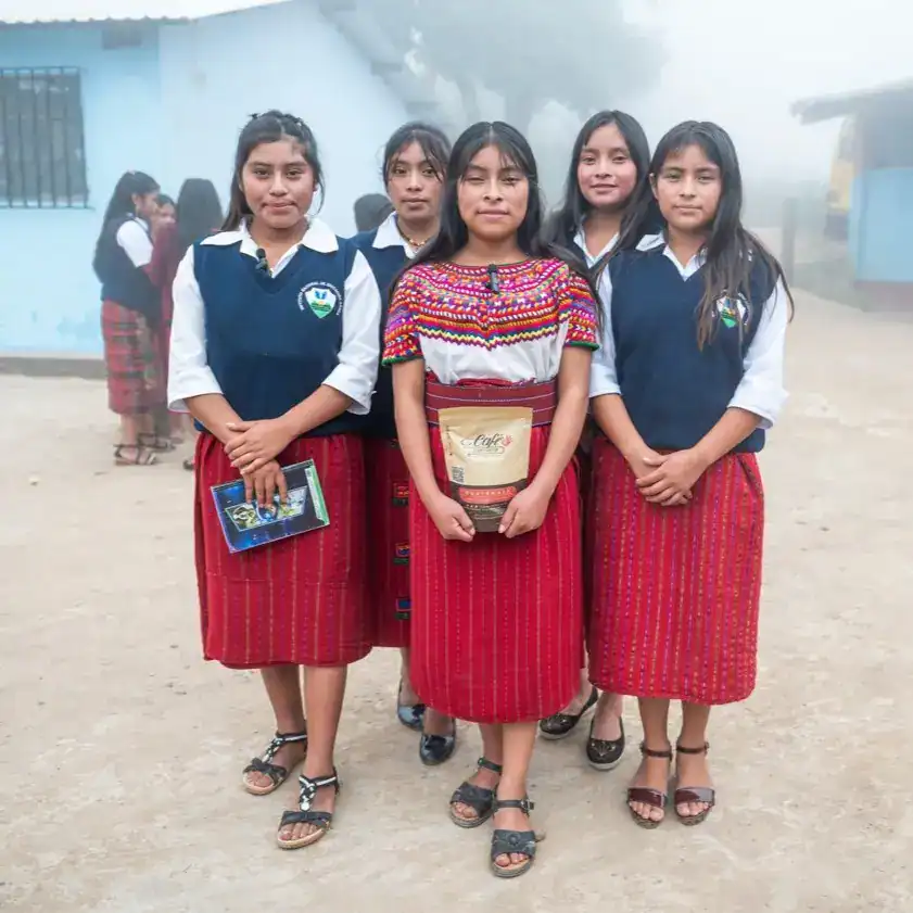 Niñas con vestimenta tradicional guatemalteca en un entorno escolar, promoviendo la cultura indígena y la educación en comunidades rurales de Guatemala. – SoyMigrante.com REVISTA