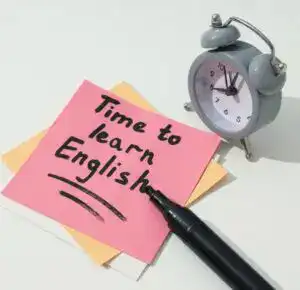 Aprender inglés, frase en notas adhesivas y reloj de alarma. – SoyMigrante.com REVISTA