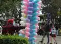 Bastón de algodón de azúcar multicolor en el parque, rodeado de personas disfrutando del evento y la feria, símbolo tradicional de dulzura y celebraciones populares en México.