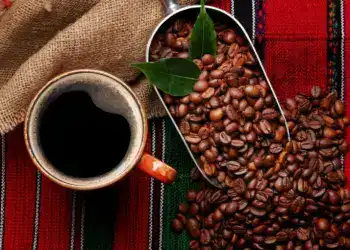 Granos de café y una taza de café negro en un fondo de tela tradicional mexicana, representando cultura y productividad en la gastronomía hispana.
