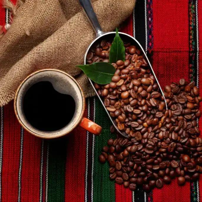Granos de café y una taza de café negro en un fondo de tela tradicional mexicana, representando cultura y productividad en la gastronomía hispana. – SoyMigrante.com REVISTA