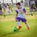 Niño jugando al fútbol en un campo al aire libre durante un partido infantil de deporte.
