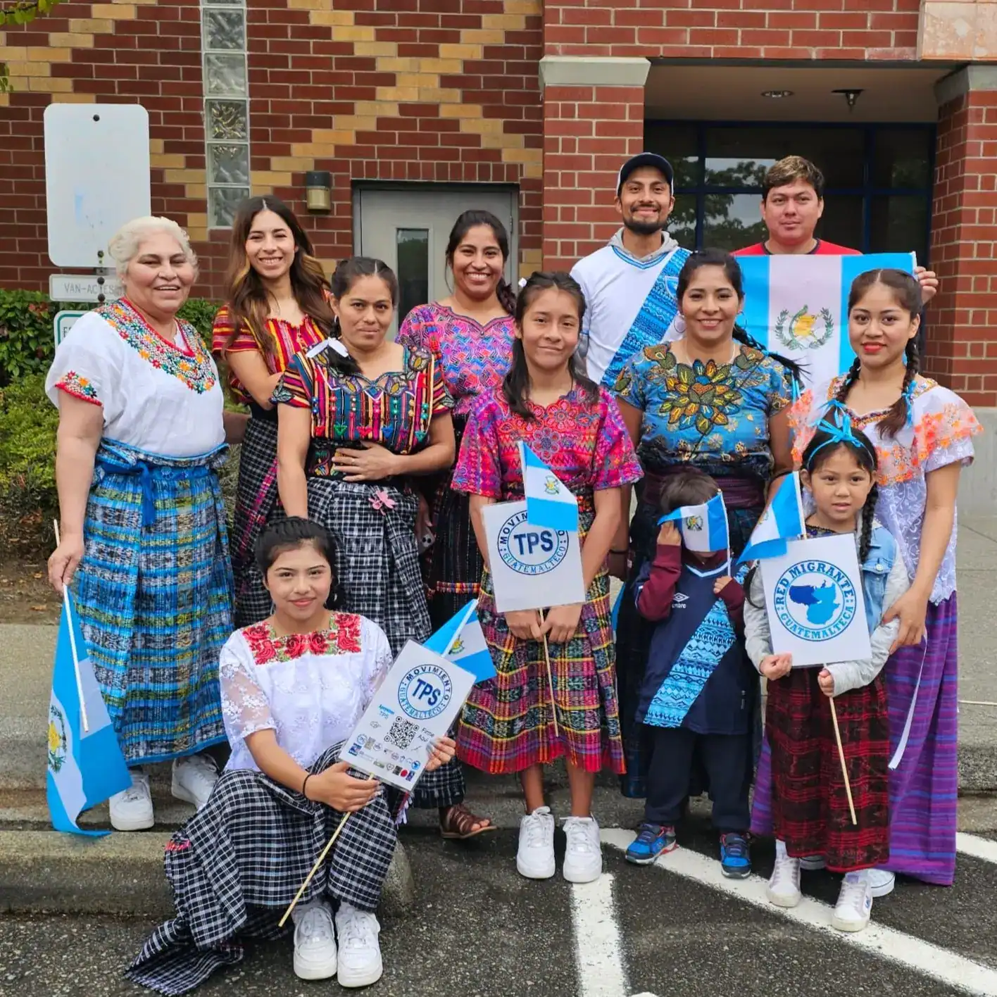 Diversidad cultural de migrantes en Guatemala celebrando con trajes tradicionales y banderas nacionales en evento comunitario.