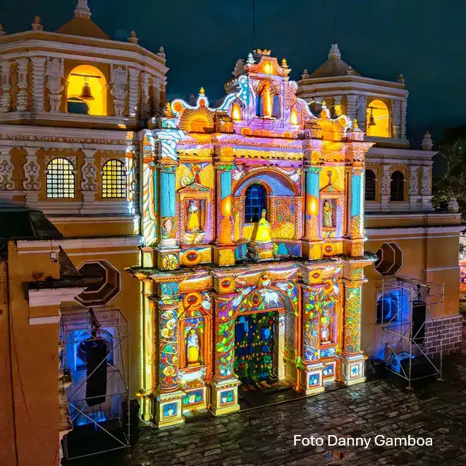Vivienda antigua decorada con proyecciones de luz y color en la noche, destacando detalles arquitectónicos y efectos visuales para eventos culturales y festivales en México. – SoyMigrante.com REVISTA