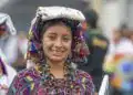 Vendedora indígena con traje tradicional colorido y accesorios en feria cultural en México, promoviendo identidad y cultura migrante.