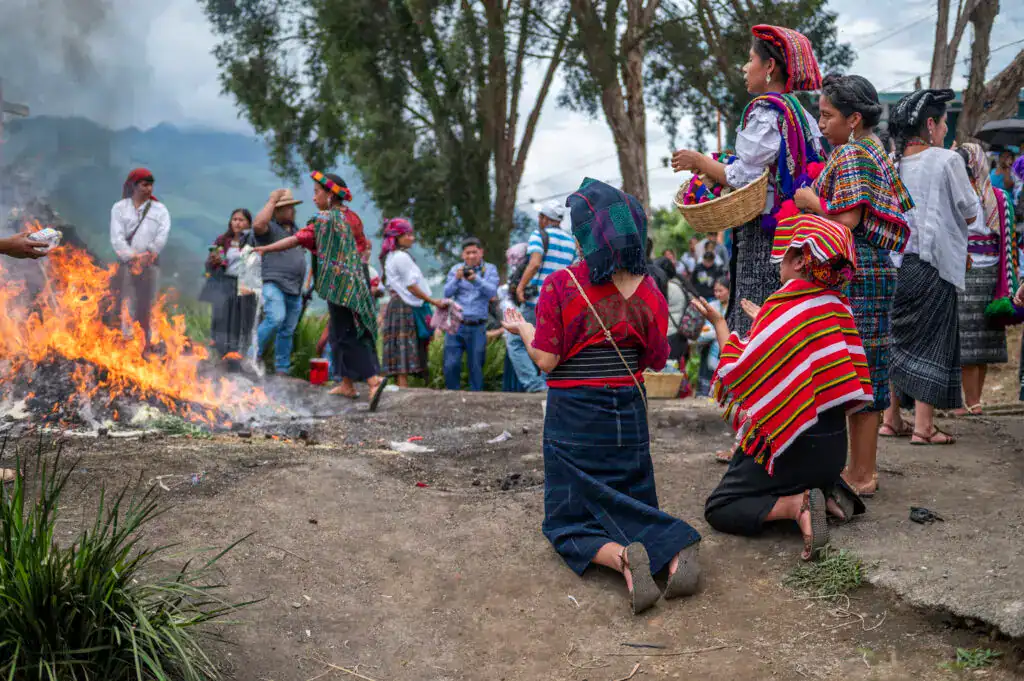Personas en ceremonia tradicional indígena con ofrenda y fuego en paisaje rural, símbolo cultural y religioso en comunidad indígena. – SoyMigrante.com REVISTA