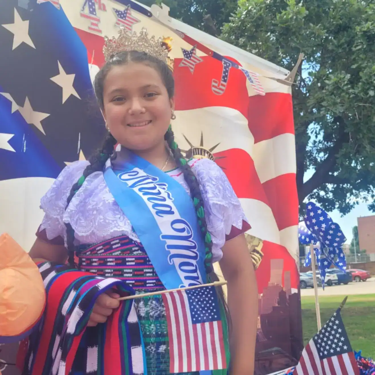 Migrantes guatemaltecos participan en desfile de independencia de Estados Unidos en Oklahoma. el 4 de juliol de 2024 – SoyMigrante.com REVISTA Niña con corona y banda azul, celebrando el Día de la Independencia de Estados Unidos, en un evento patriótico con decoración de banderas y motivos estadounidenses, en un ambiente festivo y alegre.