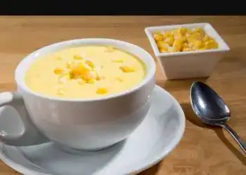 Crema de maíz en taza blanca con acompañamiento de maíz en un bol pequeño, servido en mesa de madera, ideal para recetas tradicionales y cultura hispana.
