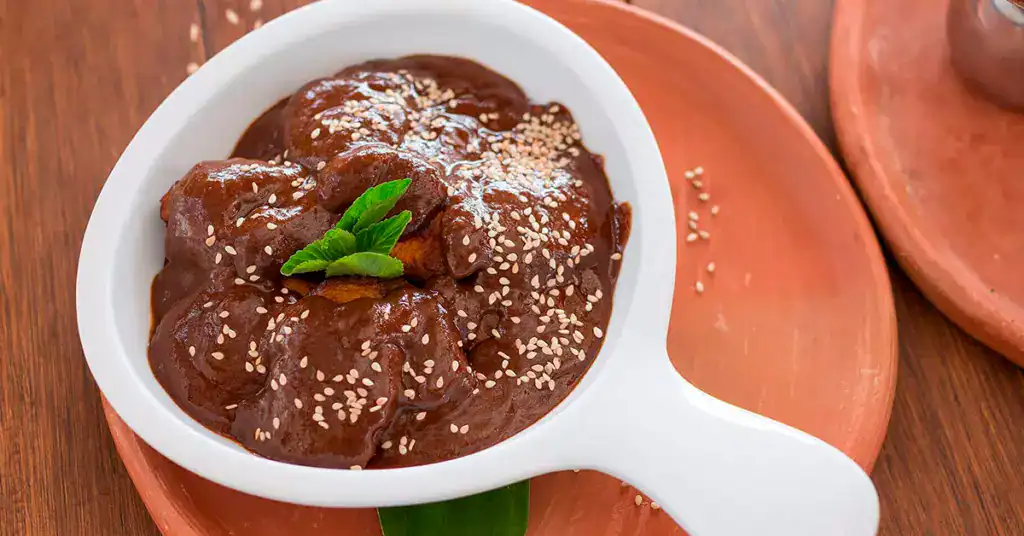 Delicioso mole tradicional servido en plato de cerámica, con semillas de sésamo y hojas de hierbabuena decorando, ideal para acompañar platillos típicos mexicanos.