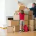 Caja de mudanza con un adulto y un niño en una vivienda, preparando para cambiar de hogar, reflejando migración y nuevas oportunidades.