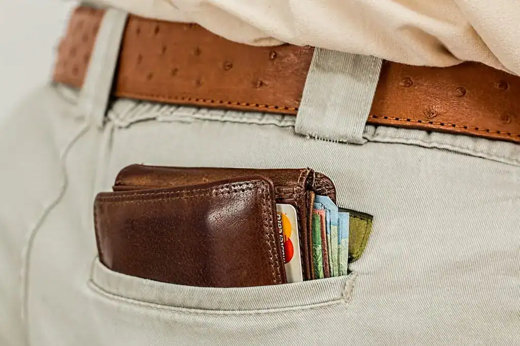 Billetera de cuero con tarjetas y dinero en el bolsillo de unos pantalones claros, representando temas de migración y finanzas.
