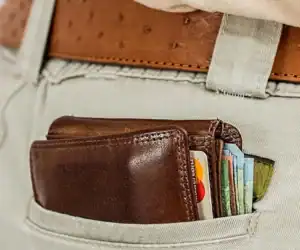 Billetera de cuero con tarjetas y dinero en el bolsillo de unos pantalones claros, representando temas de migración y finanzas.
