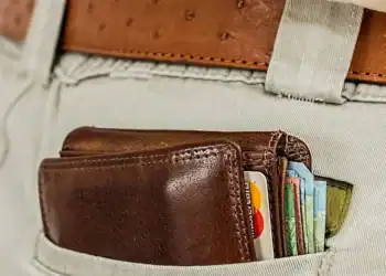 Billetera de cuero con tarjetas y dinero en el bolsillo de unos pantalones claros, representando temas de migración y finanzas.