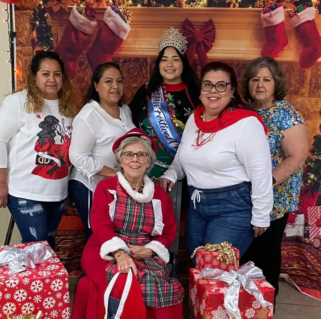 Diversas mujeres en celebración navideña con temática de época navideña y premios, destacando la comunidad migrante y festividades culturales.