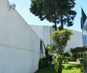 México, bandera mexicana en un espacio público con vegetación y señalética, símbolo de cultura y orgullo nacional en un entorno verde y luminoso. – SoyMigrante.com REVISTA