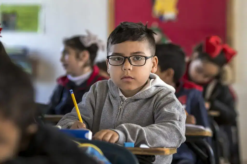 Estudiante en aula escolar, niño con gafas, atención y concentración en clase, educación, aprendizaje, escuela primaria. – SoyMigrante.com REVISTA