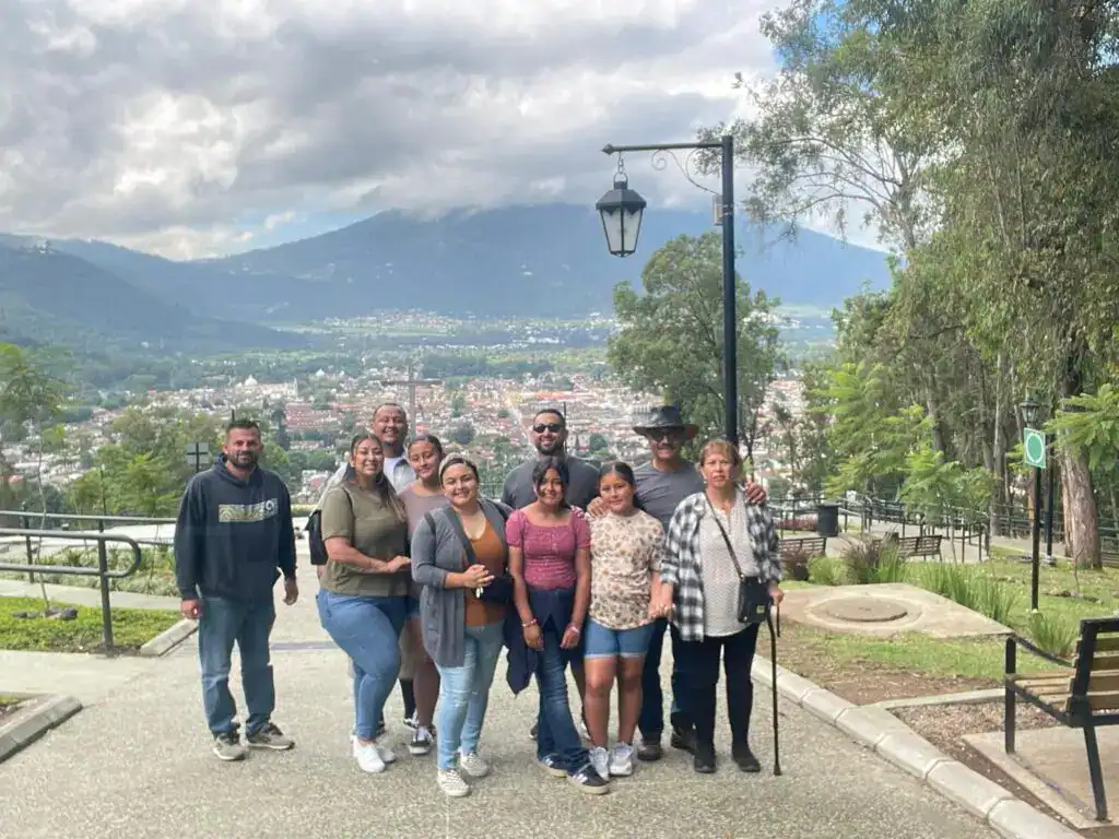 Paseo en grupo de migrantes en un parque con vista panorámica de la ciudad y montañas, promoviendo la integración y cultura migrante en un entorno natural y seguro. – SoyMigrante.com REVISTA