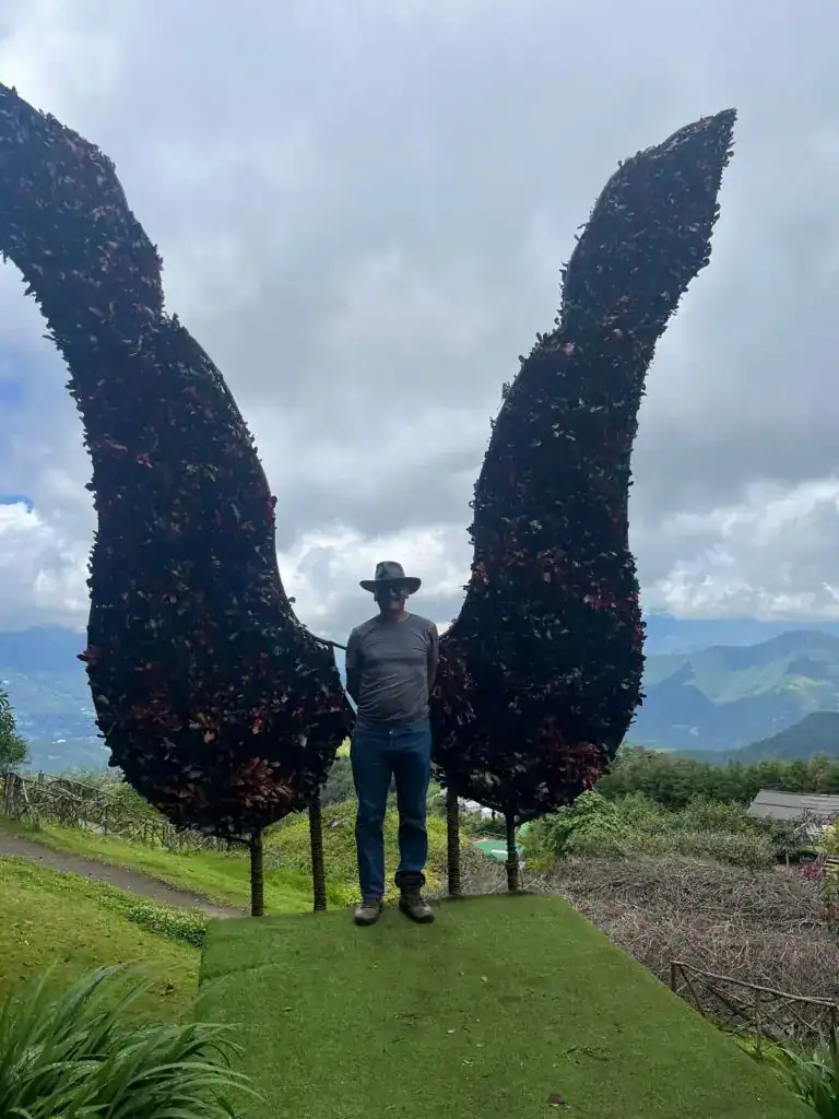 Vendedor de café en la Sierra de Chiapas, México, con gran escultura de hojas de café, representando la cultura y el trabajo agrícola de los migrantes y productores de café en la región. – SoyMigrante.com REVISTA