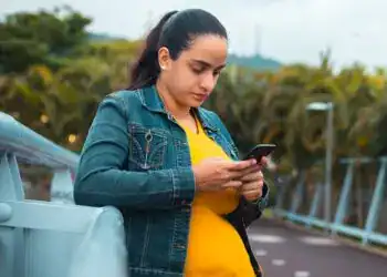 SoyMigrante.com revista, mujer embarazada utilizando su teléfono en la calle, promoviendo la participación de migrantes y temas relevantes en movilidad internacional y derechos en América Latina.