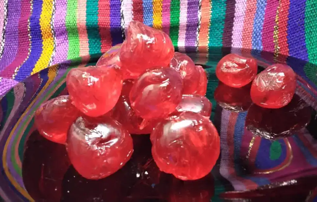 Dulces mexicanos de fruta en forma de bolas rojas transparentes sobre tela mexicana colorida. – SoyMigrante.com REVISTA