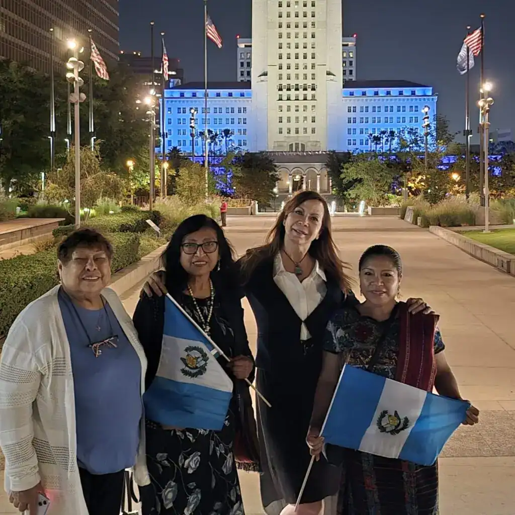 Vestido con bandera de Guatemala, grupo en acto cívico, celebración cultura guatemalteca, ciudad de Los Ángeles, noche, mujeres inmigrantes guatemaltecas, orgullo cultural, comunidad migrante, evento patriótico, actividad social.