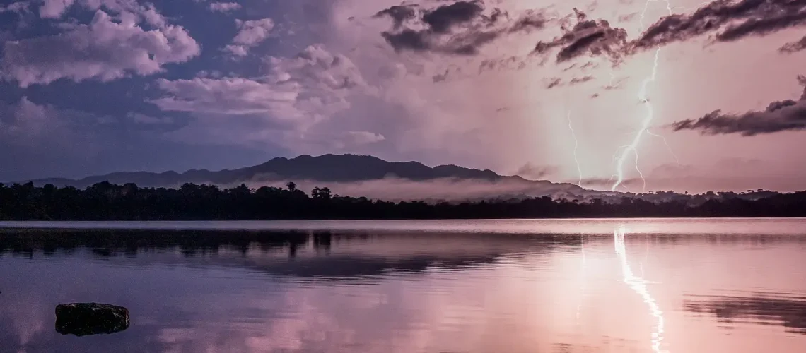 Relámpagos iluminando un lago tranquilo al atardecer, reflejando un cielo dramatico con nubes y relámpagos, en un paisaje natural impresionante.