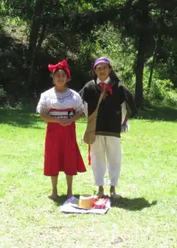 Jovenes con indumentaria akateko, participando en una celebración cultural al aire libre en un entorno natural. Idioma y etnia maya akateko o maya akateka