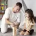 Hombre y niña jugando a un juego de apilamiento con bloques de madera en un ambiente familiar y acogedor.