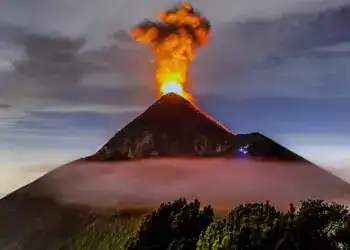 Vista del volcán en erupción con columnas de humo y lava illuminated por la noche, símbolo del poder de la naturaleza y la actividad volcánica en América Central.
