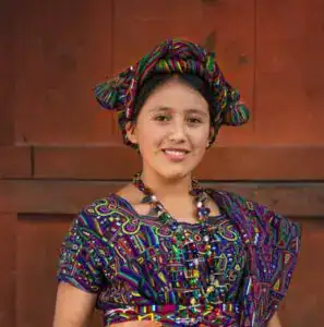 Niña indígena con vestimenta tradicional y accesorios coloridos, representando cultura y identidad en comunidades migrantes en América Latina.
