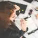 Estudiante trabajando en el ordenador con material de estudio y café, en un ambiente de oficina o estudio.
