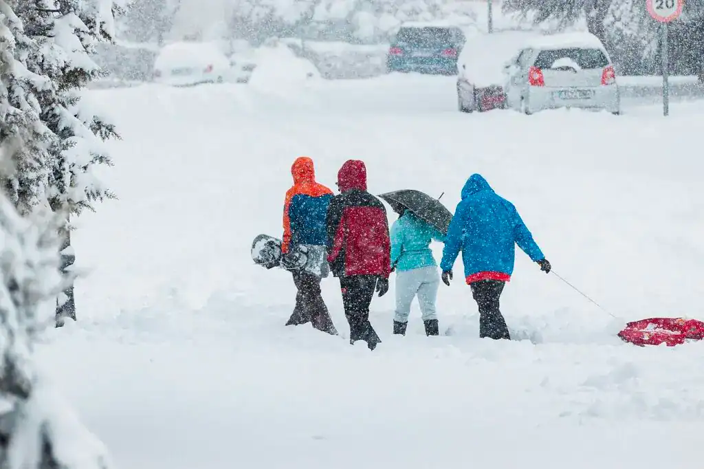 Nieve y personas con ropa de invierno caminando en una calle cubierta de nieve en un día de tormenta. – SoyMigrante.com REVISTA