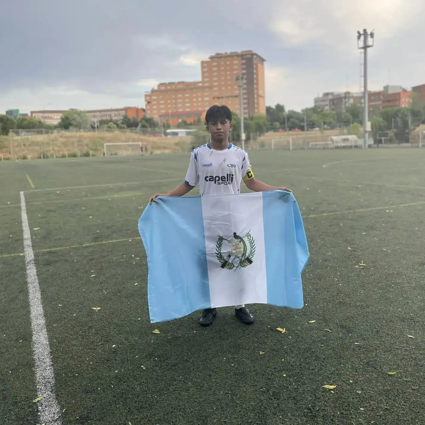 Juventud futbolista con bandera de Guatemala en campo de fútbol, promoviendo el deporte y la cultura migrante en Estados Unidos.