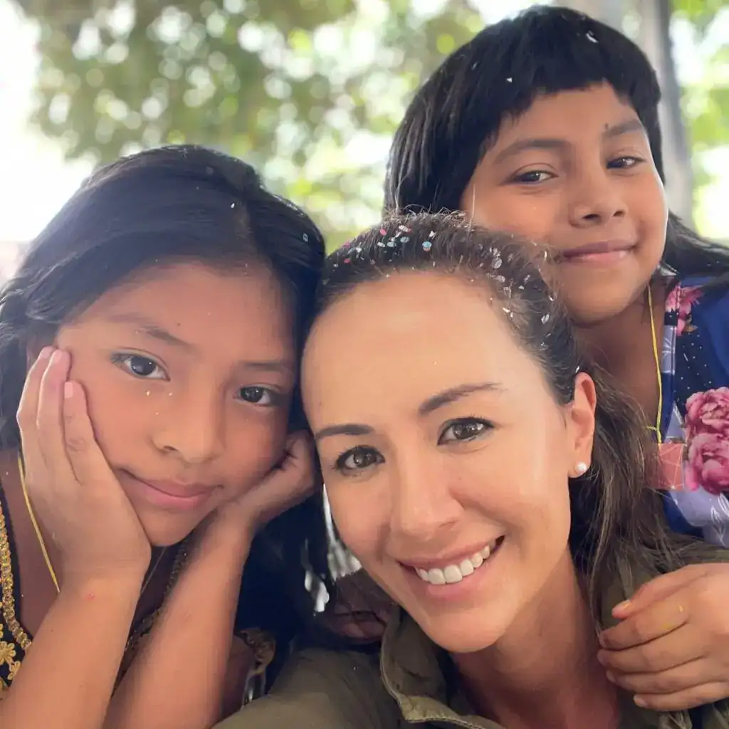 Niños y una mujer sonrientes en un entorno natural, promoviendo la visión de comunidad y bienestar en migrantes y sus familias en la revista SoyMigrante.com REVISTA. – SoyMigrante.com REVISTA